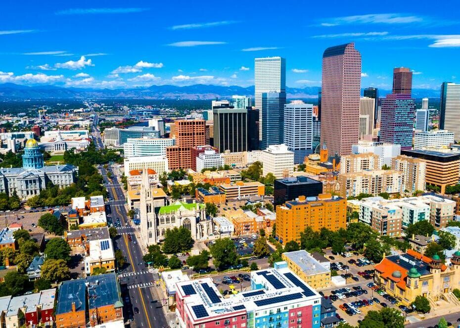 Downtown Denver, Colorado against a blue sky with mountains in the distance.